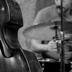 A black-and-white photo of a drummer, drumkit and double bass.